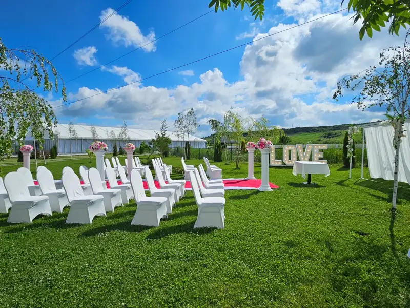 Zona de ceremonie din grădină, cu scaune albe și decor LOVE